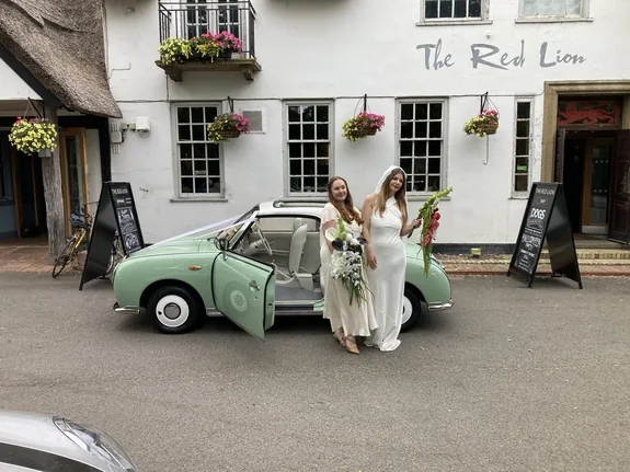 Two brides with a Nissan Figaro wedding car outside The Red Lion, Grantchester, Cambridge