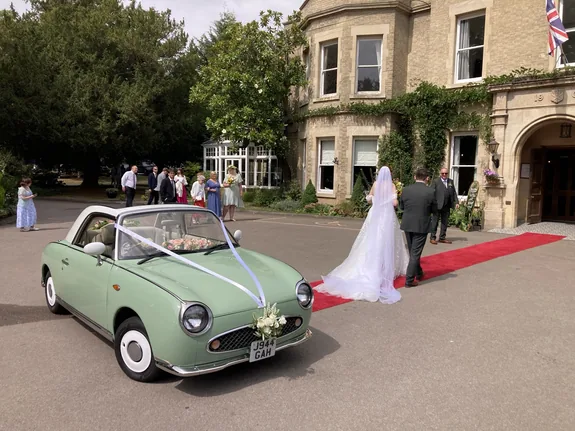 Bride arriving at Woodland Manor, Bedford, in a classic Nissan Figaro wedding car