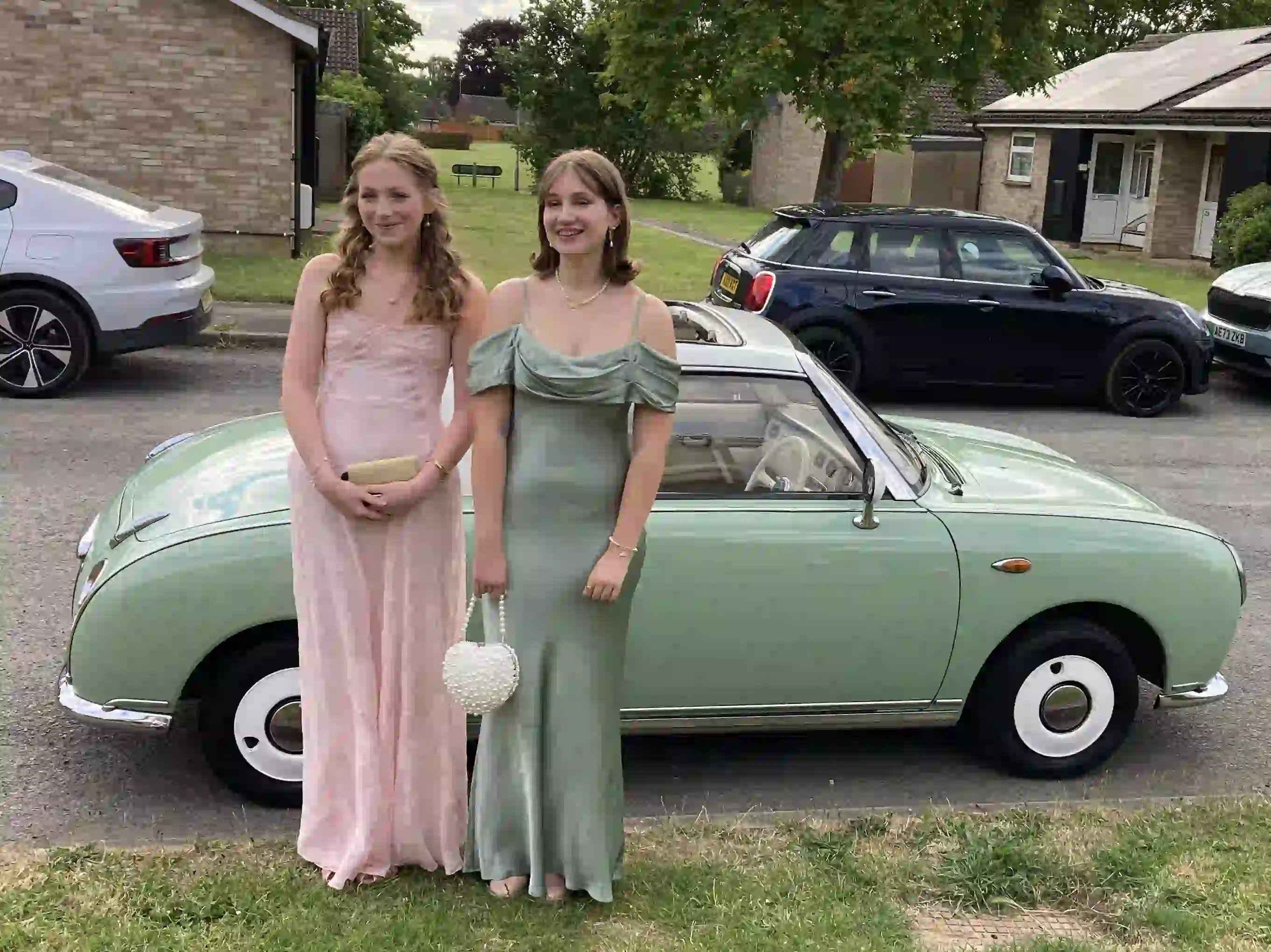 Jessica and Imogen in prom dresses in front of a Nissan Figaro prom car