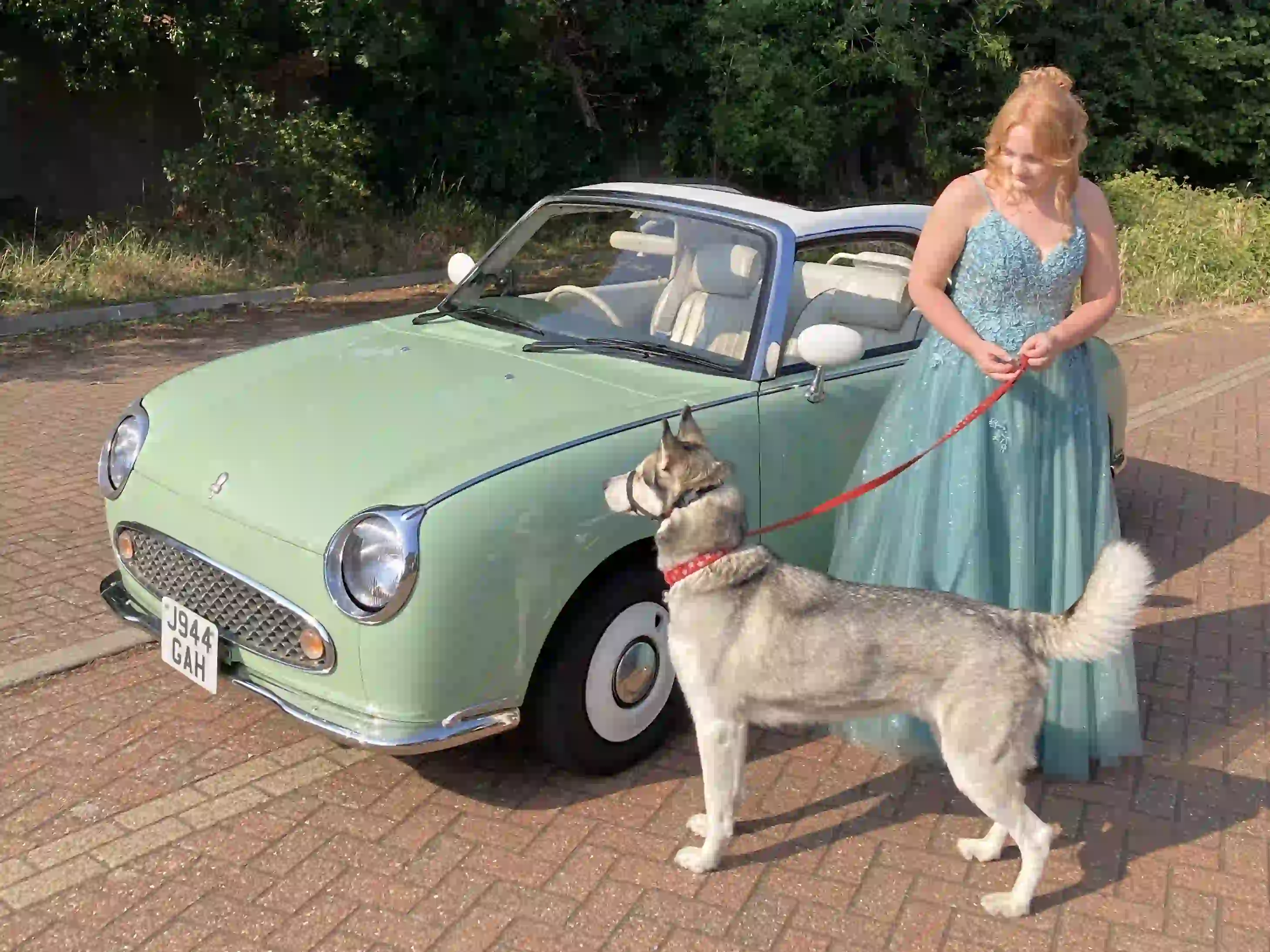 Hollie in her prom dress beside a Nissan Figaro prom car with her dog before her Norwich prom