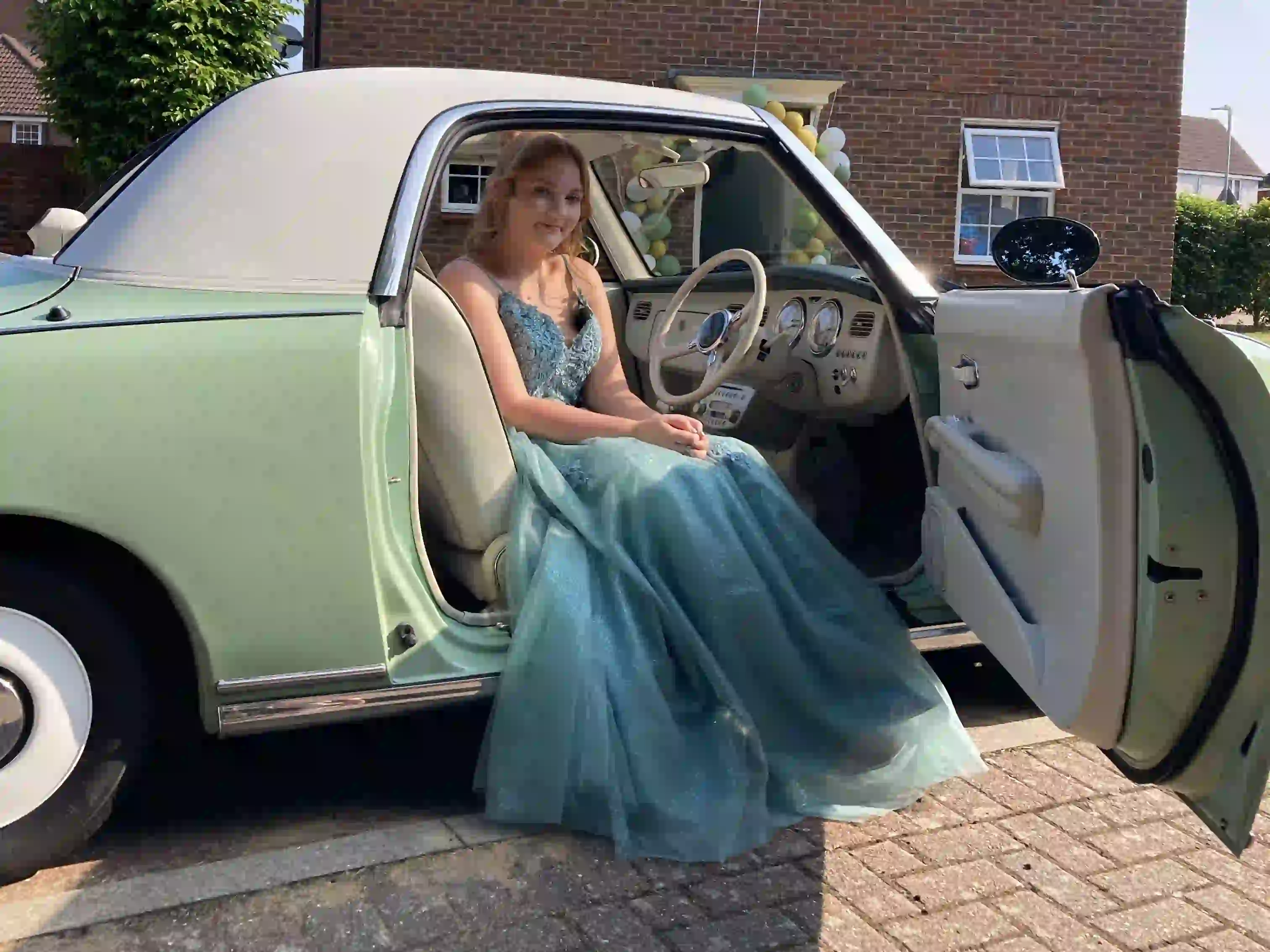Hollie in the driver's seat of a Nissan Figaro prom car, steering wheel and dashboard visible, before her Norwich prom