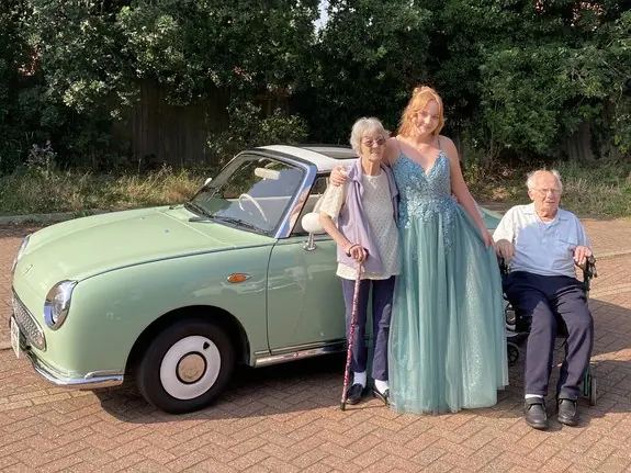 Girl in a prom dress with her family beside a Nissan Figaro prom car