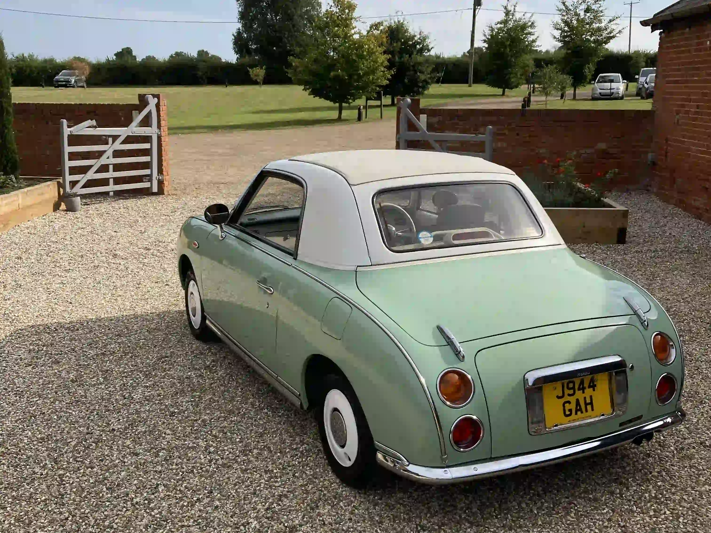 Rear view of a mint green Nissan Figaro prom car parked on a gravel drive near Woodbridge
