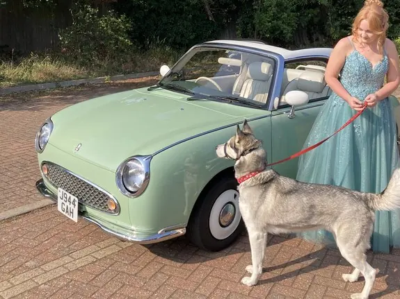 Girl in a prom dress with a dog beside a Nissan Figaro prom car